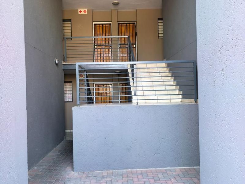 Exterior view of an apartment complex entrance featuring a paved walkway, staircase with metal balustrades, and secure unit access points.