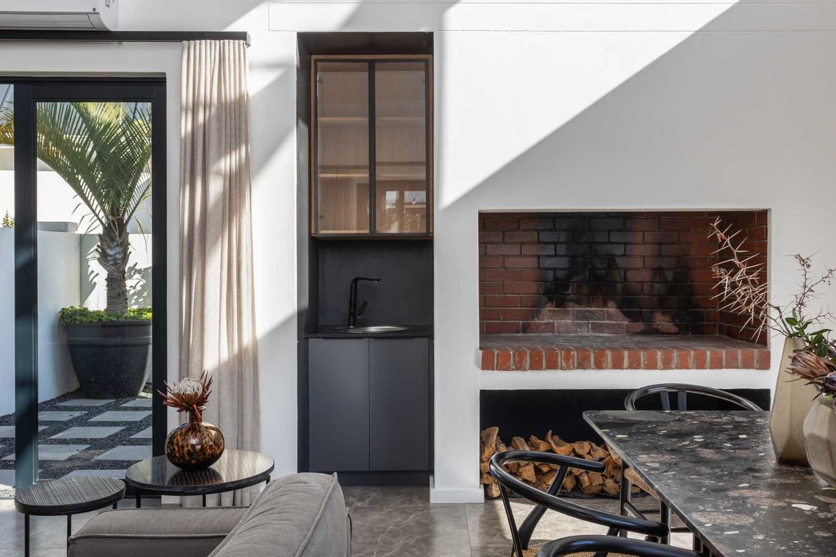 Modern living area featuring a built-in brick fireplace, sleek dark cabinetry with an integrated sink, and large sliding doors opening to a patio.