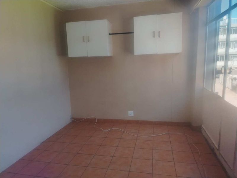An empty bedroom featuring tiled flooring, wall-mounted storage cabinets, and a large window providing natural light.