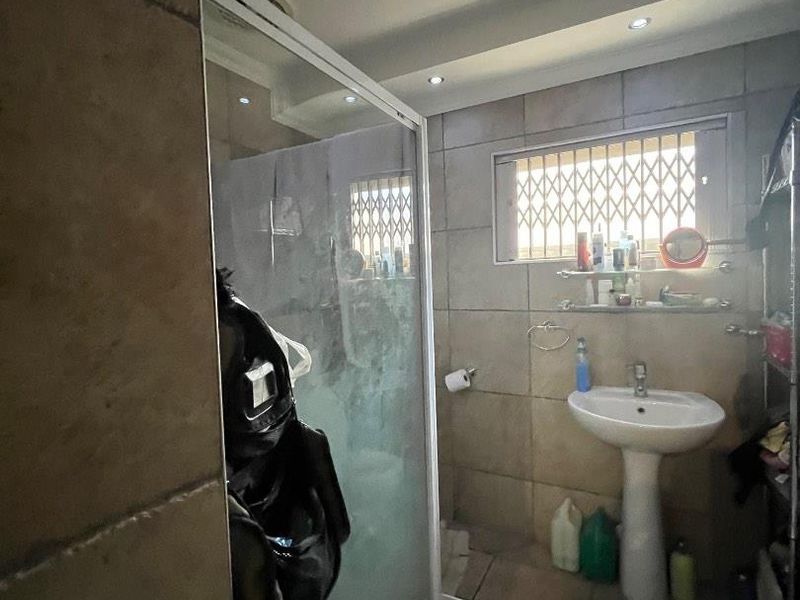 A functional bathroom featuring a pedestal basin, tiled finishes, and a glass shower enclosure with recessed lighting.
