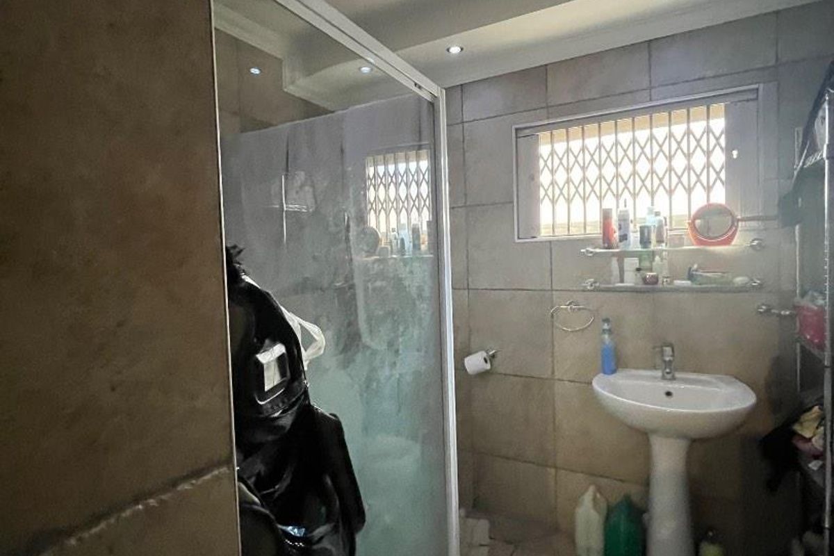 A functional bathroom featuring a pedestal basin, tiled finishes, and a glass shower enclosure with recessed lighting.