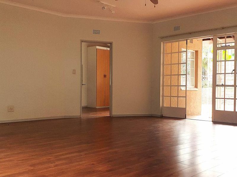 Spacious, empty living room featuring laminate flooring, a ceiling fan, and large sliding glass doors providing access to the outdoor area.