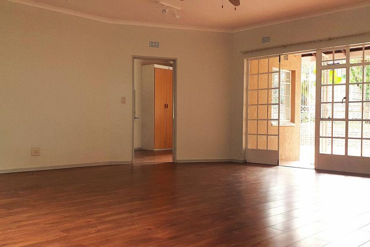 Spacious, empty living room featuring laminate flooring, a ceiling fan, and large sliding glass doors providing access to the outdoor area.