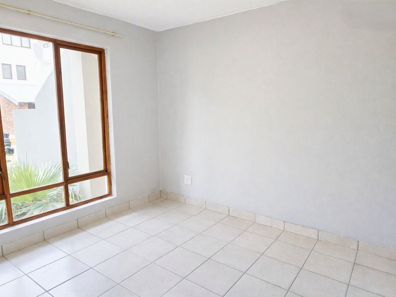 A bright, empty bedroom featuring neutral tiled flooring and a large timber-framed window, providing a clean canvas for personalization.