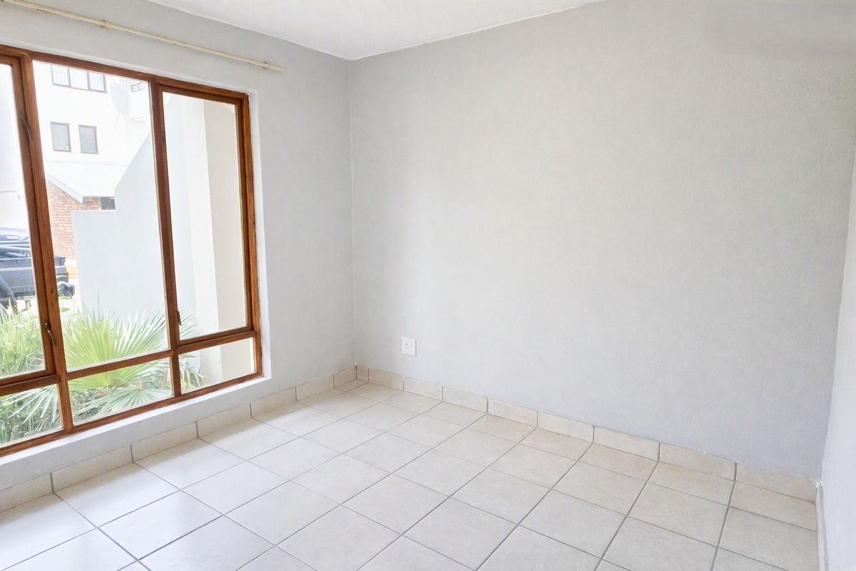 A bright, empty bedroom featuring neutral tiled flooring and a large timber-framed window, providing a clean canvas for personalization.