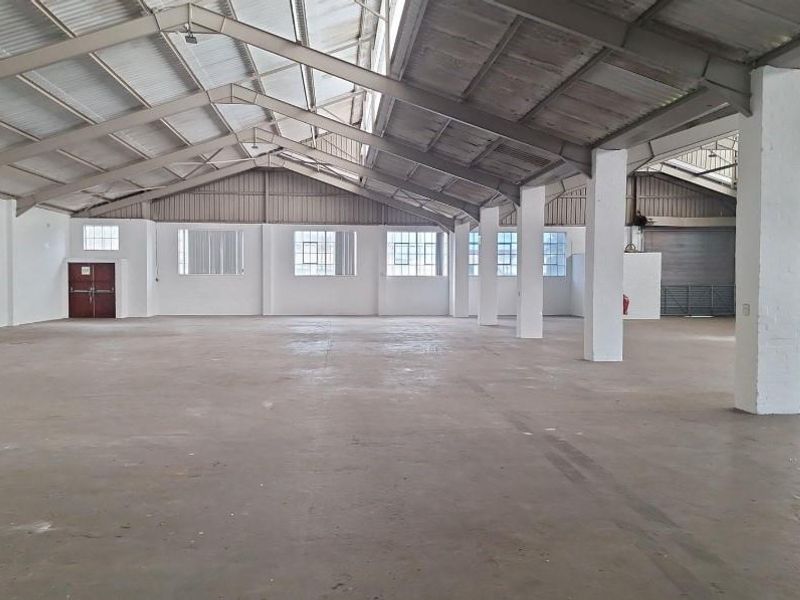 Spacious industrial warehouse featuring high ceilings with exposed steel trusses, concrete flooring, and ample natural light through multiple windows.