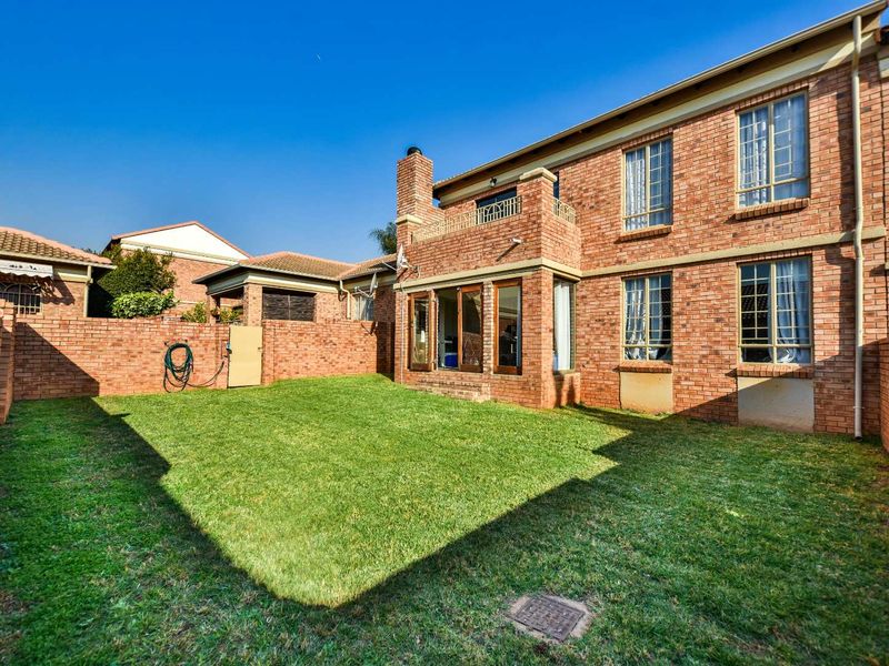 Rear view of the townhouse featuring a private garden with a lawn, brick boundary walls, and a balcony accessible from the upper level.