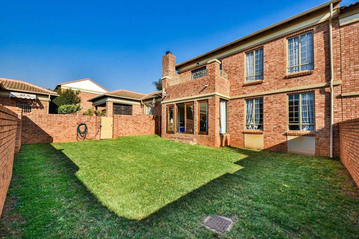 Rear view of the townhouse featuring a private garden with a lawn, brick boundary walls, and a balcony accessible from the upper level.