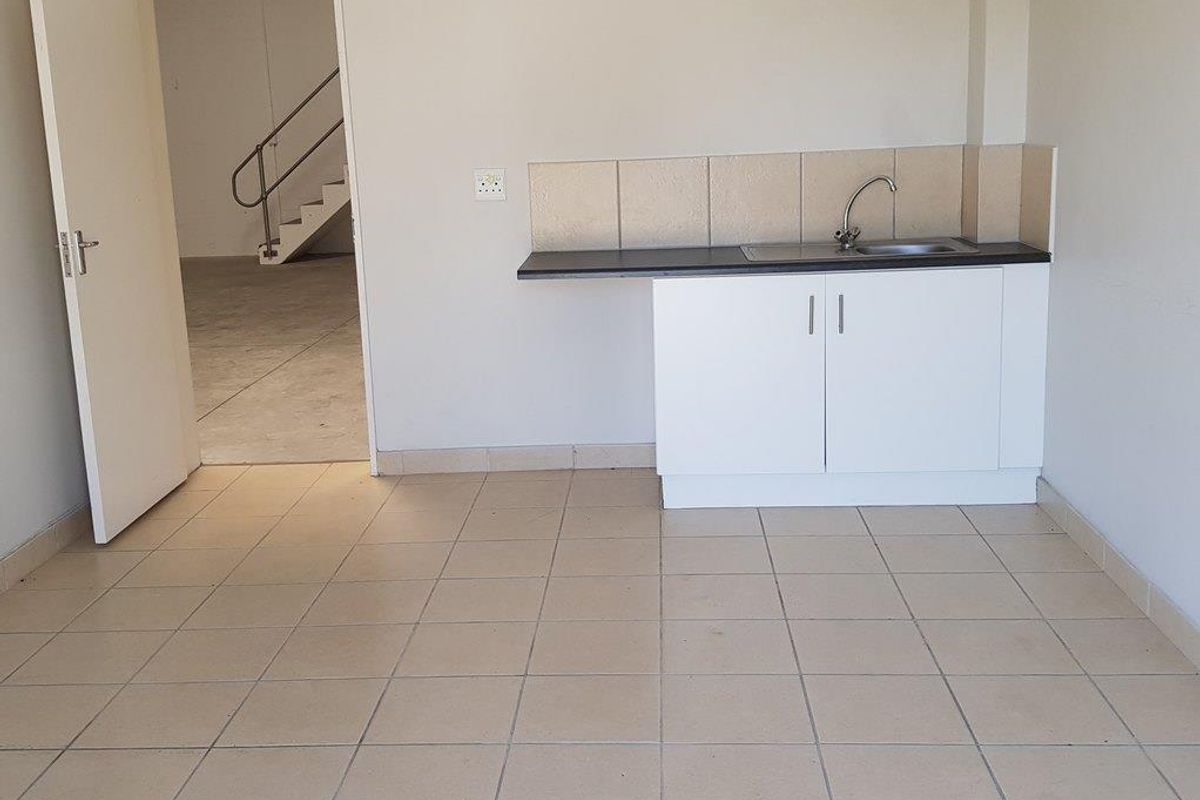 A functional kitchenette area featuring a single sink, white cabinetry, and tiled flooring, with an adjacent doorway leading to a staircase.