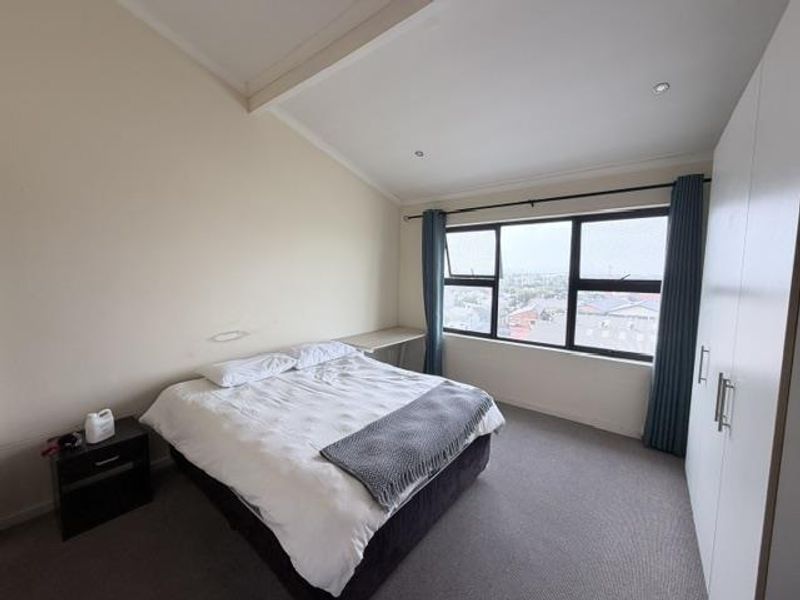 A bright bedroom featuring a sloped ceiling, built-in wardrobe, and a large window offering elevated views.