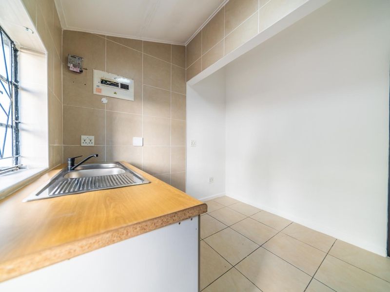 A functional kitchen area featuring a stainless steel sink, laminate countertop, tiled backsplash, and tiled flooring, with an integrated electrical distribution board.