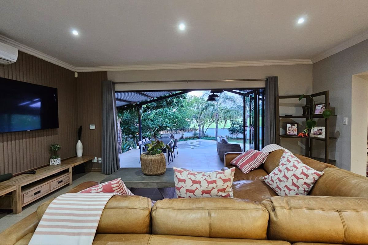 Spacious living room featuring modern timber-look wall paneling, recessed lighting, and large stacking glass doors that open onto an outdoor patio area.