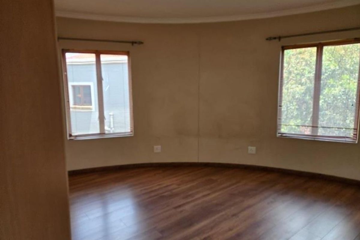 An empty bedroom featuring laminate wood flooring and two windows with blinds, showing signs of wall wear and staining.