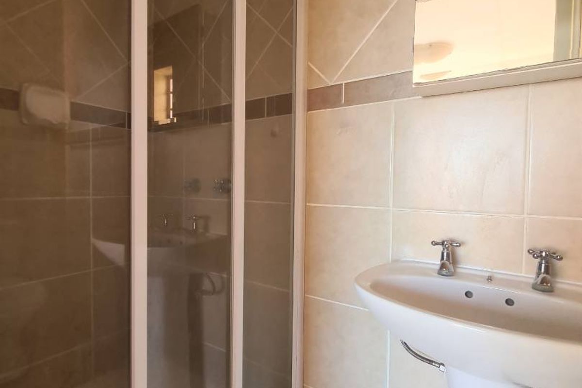A functional bathroom featuring a pedestal basin, a shower enclosure with sliding doors, and neutral wall and floor tiling.