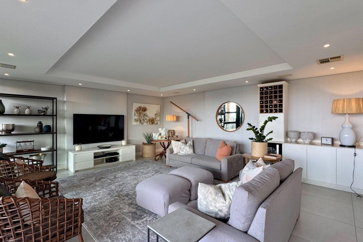 Spacious living room featuring a modern recessed ceiling with downlights, built-in cabinetry, and a dedicated wine storage unit, finished with neutral tiled flooring.