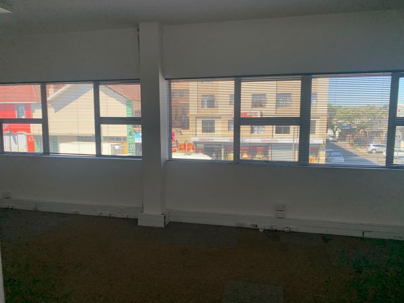An empty office space featuring large windows with venetian blinds, carpeted flooring, and integrated electrical outlets, offering a functional workspace with street views.