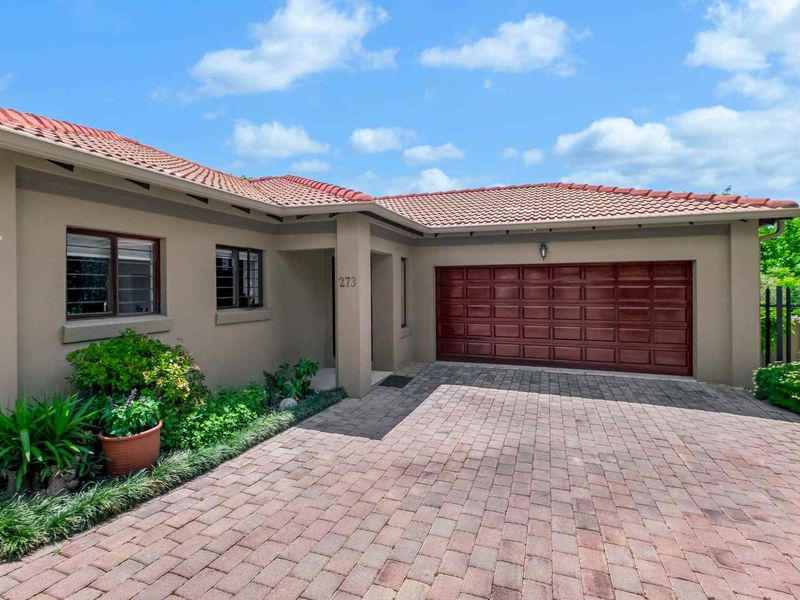 Front elevation of a well-maintained house featuring a paved driveway, a sectional garage door, and tiled roofing.
