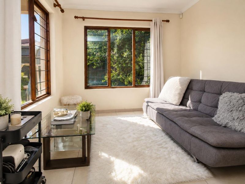 A bright and airy living room featuring tiled flooring, timber-framed windows with security bars, and classic cornicing, offering a comfortable and well-lit space.