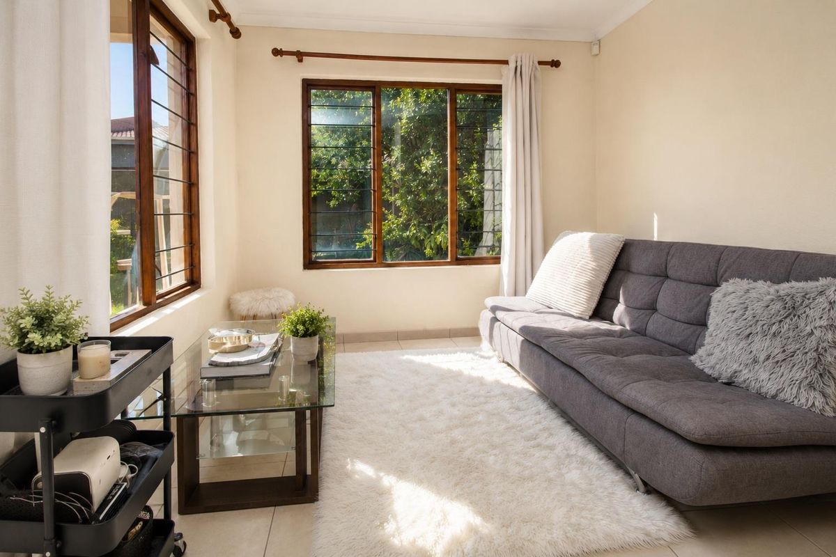 A bright and airy living room featuring tiled flooring, timber-framed windows with security bars, and classic cornicing, offering a comfortable and well-lit space.