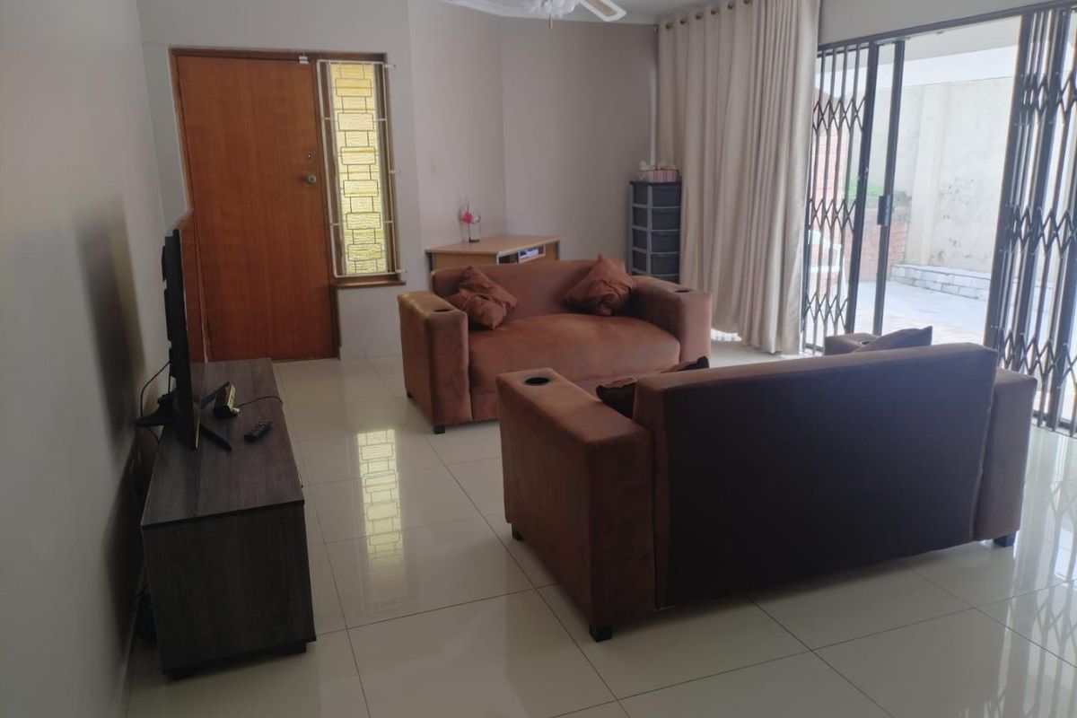 A living room featuring tiled flooring, a ceiling fan, and a sliding glass door with a security gate leading to the exterior.