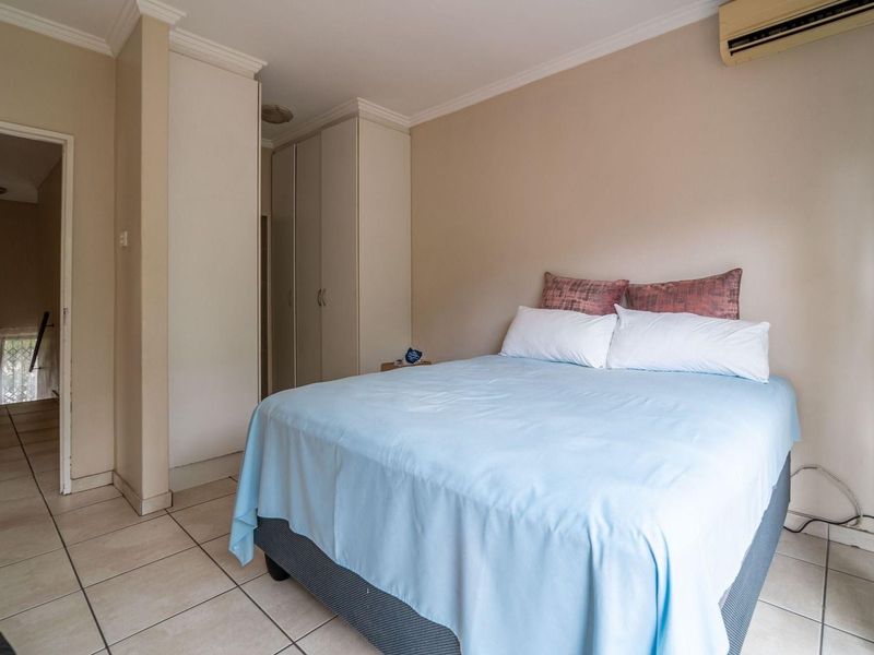 A functional bedroom featuring built-in cupboards, tiled flooring, and a wall-mounted air conditioning unit.