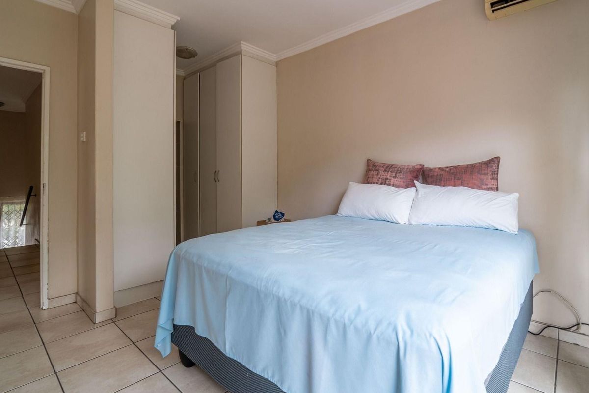 A functional bedroom featuring built-in cupboards, tiled flooring, and a wall-mounted air conditioning unit.