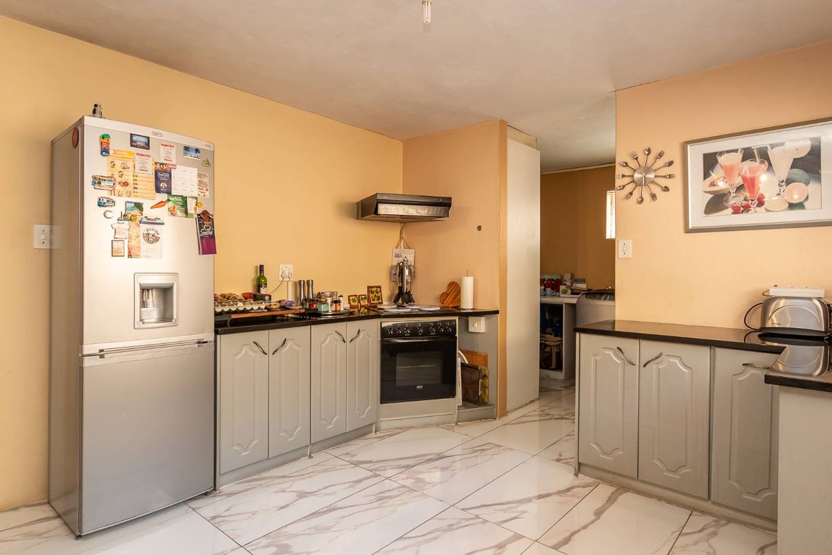 A functional kitchen featuring light grey cabinetry, dark countertops, a built-in oven with extractor fan, and modern marble-look floor tiles.