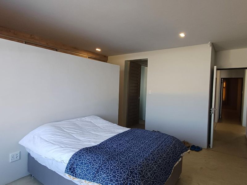 A spacious bedroom featuring neutral walls, recessed downlighting, and integrated built-in cupboards, providing a clean and functional living space.
