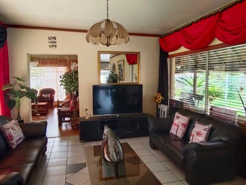 A living room featuring tiled flooring, large windows with venetian blinds, and a central ceiling light fixture, providing a functional and well-lit living space.