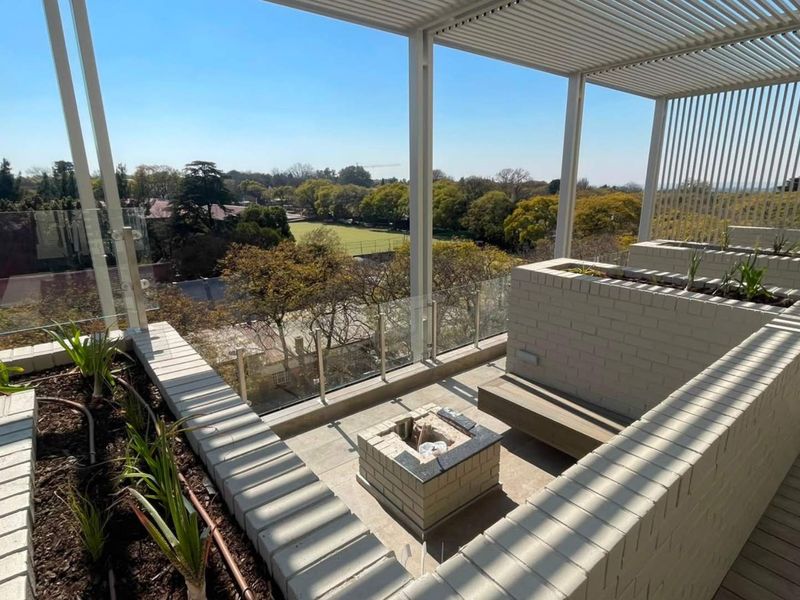 Spacious rooftop balcony featuring a modern louvred pergola, built-in brick planters, integrated fire pit, and glass balustrades with panoramic views.