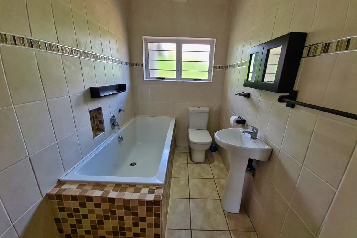 A clean, functional bathroom featuring a bathtub, pedestal sink, toilet, and neutral wall tiling with decorative mosaic accents.