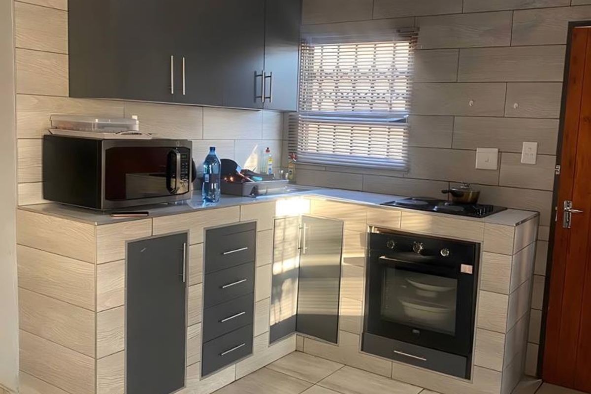 A compact kitchen featuring modern grey cabinetry, built-in oven, electric hob, and wood-look tiled finishes throughout.