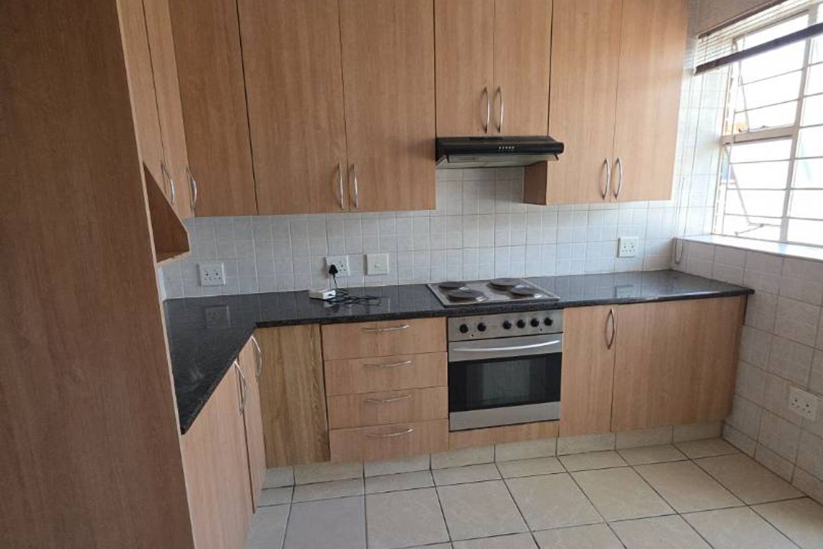 A functional kitchen featuring light wood-look cabinetry, granite countertops, built-in oven, and hob, finished with ceramic floor tiles and a tiled backsplash.