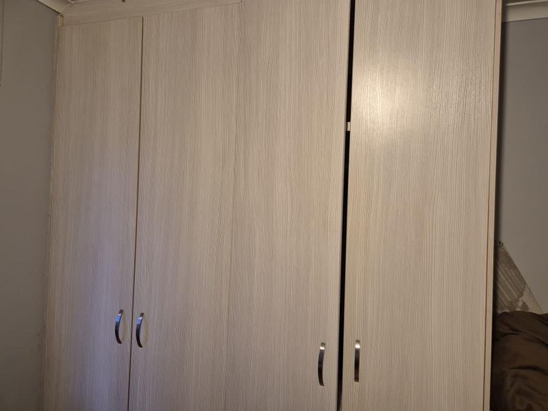 A bedroom featuring a large, light-wood grain built-in wardrobe with modern metal handles.