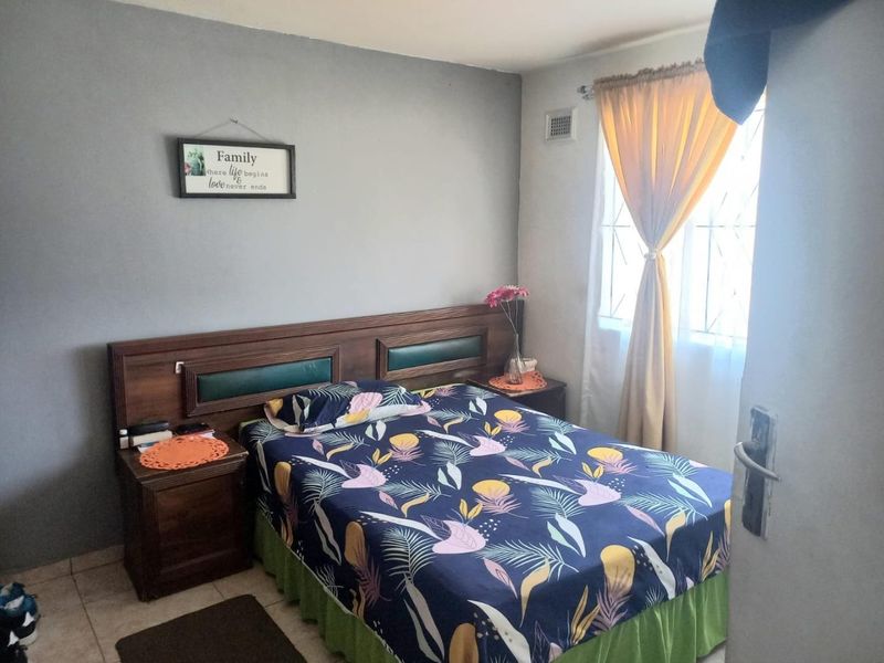 A functional bedroom featuring tiled flooring, a built-in wooden headboard, and a window fitted with a security gate.