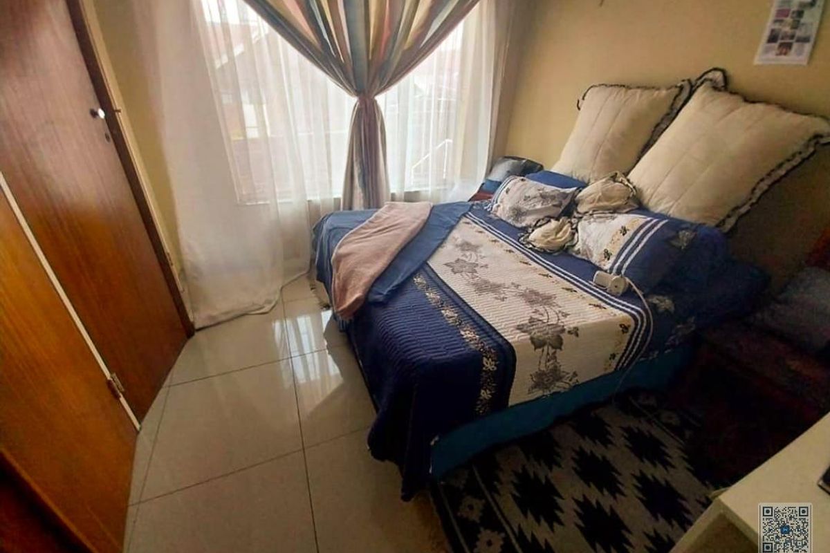 A compact bedroom featuring tiled flooring, a built-in wooden door, and large window with curtains, providing a functional living space.