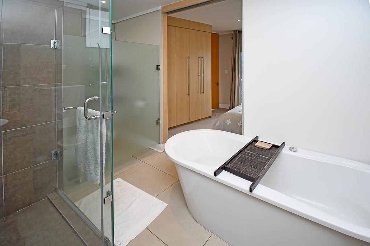 Modern en-suite bathroom featuring a freestanding bathtub, glass-enclosed shower, and tiled flooring, with direct access to the bedroom area.