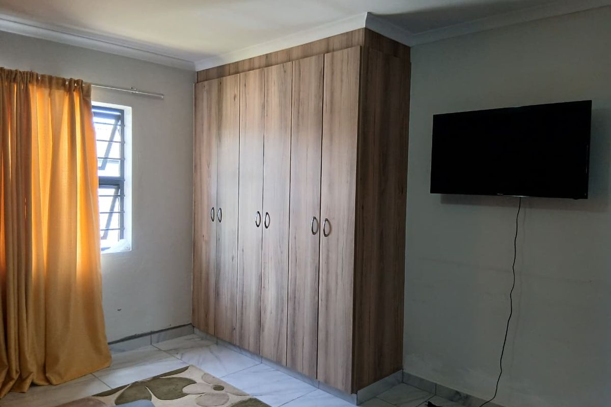 A bedroom featuring built-in wooden cupboards, tiled flooring, and a wall-mounted television.