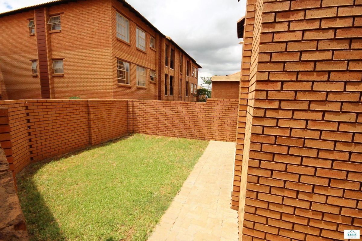 A private rear garden area featuring a brick boundary wall, a paved walkway, and a small lawn section adjacent to the apartment building.
