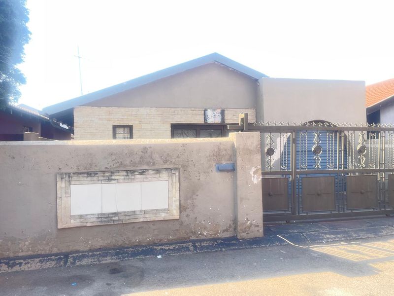 Front elevation of a residential property featuring a boundary wall with metal security gate and stone cladding accents.