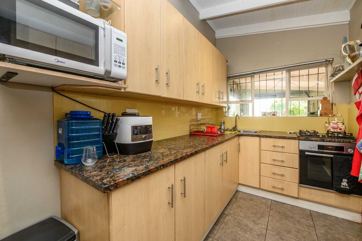 Functional kitchen featuring light wood cabinetry, granite countertops, built-in oven, gas hob, and a yellow glass splashback.