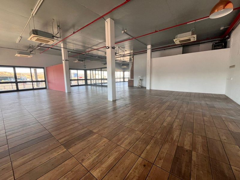 Spacious open-plan retail area featuring exposed industrial ceilings, cassette air conditioning, large windows for natural light, and durable tiled flooring.