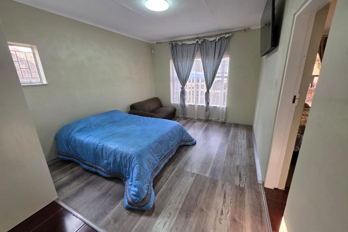 A bedroom featuring laminate flooring, neutral walls, and window security bars, providing a functional space with natural light.