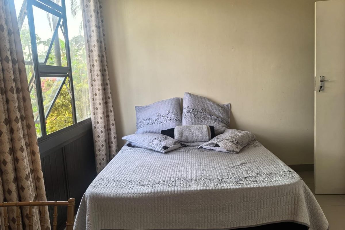 A bedroom featuring tiled flooring and a large window providing natural light and garden views.