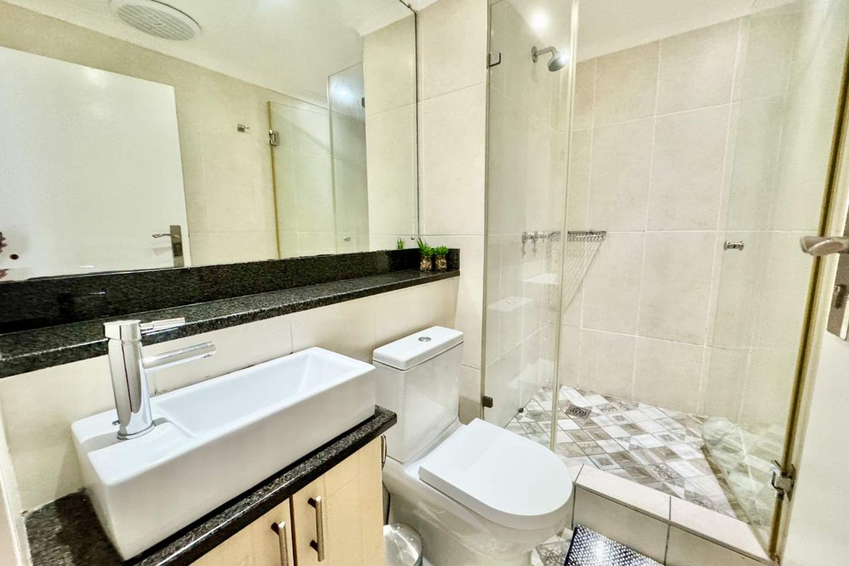 Modern bathroom featuring a glass-enclosed shower, vessel sink with granite vanity top, and neutral wall tiling.