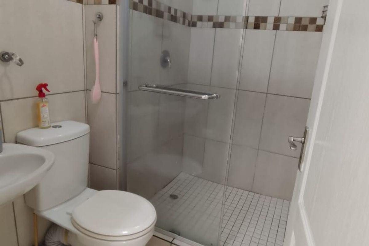 A functional bathroom featuring a pedestal basin, toilet, and a glass-enclosed shower with tiled finishes.