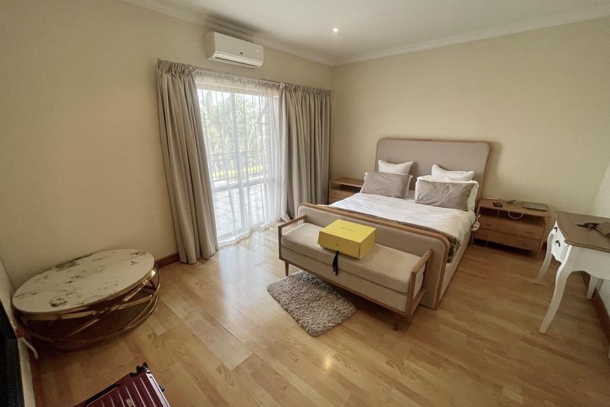 Spacious bedroom featuring light wood flooring, a wall-mounted air conditioning unit, and large sliding glass doors leading to an outdoor area.