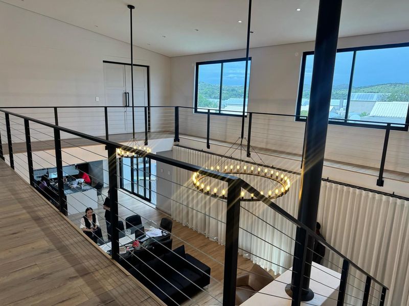 Spacious double-volume living area featuring a mezzanine level, modern cable railing, large windows, and elegant feature chandeliers.