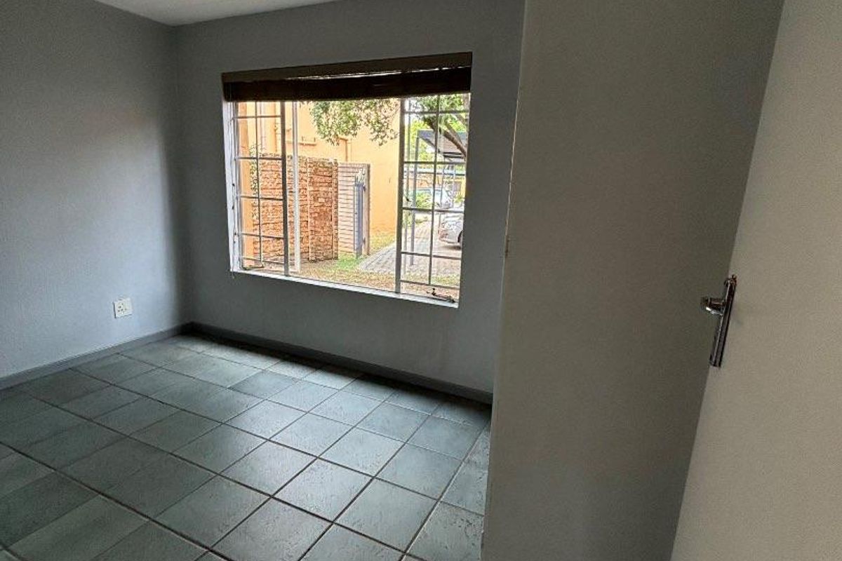 An empty bedroom featuring neutral grey walls, dark tiled flooring, and a steel-framed window with a roller blind.