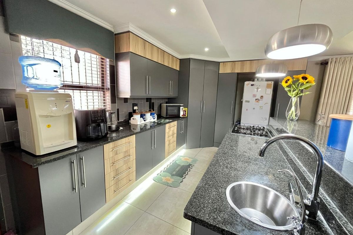 Modern kitchen featuring two-tone cabinetry, granite countertops, a breakfast bar, integrated gas hob, and recessed under-cabinet lighting.